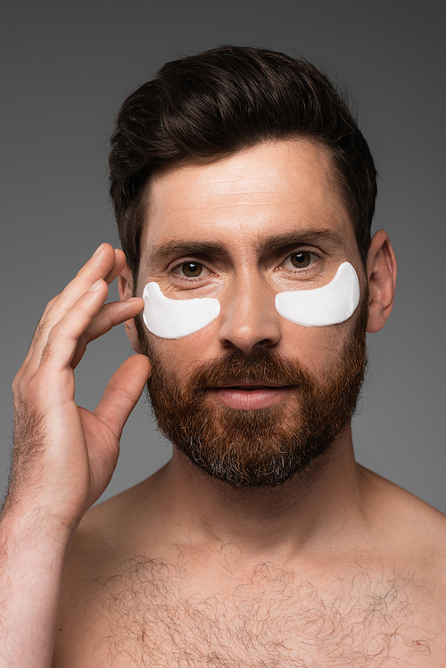 portrait of bearded man with moisturizing eye patches isolated on grey