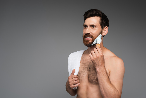 happy bearded man with towel applying shaving foam with shaving brush isolated on grey