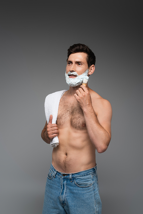 shirtless man in jeans applying white shaving foam on face on grey