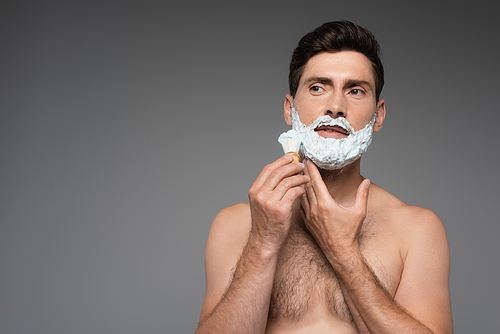 shirtless man applying white shaving foam on face on grey