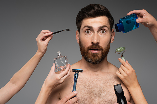 women holding beauty products around bearded and surprised man on grey