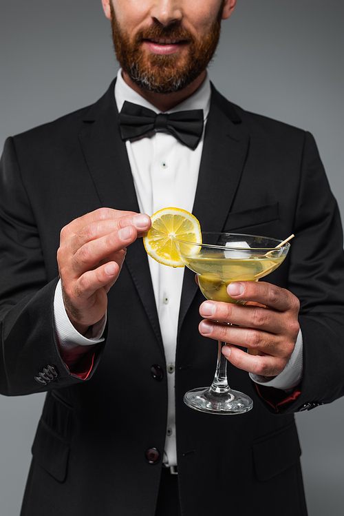 cropped view of bearded man in suit holding glass with cocktail isolated on grey