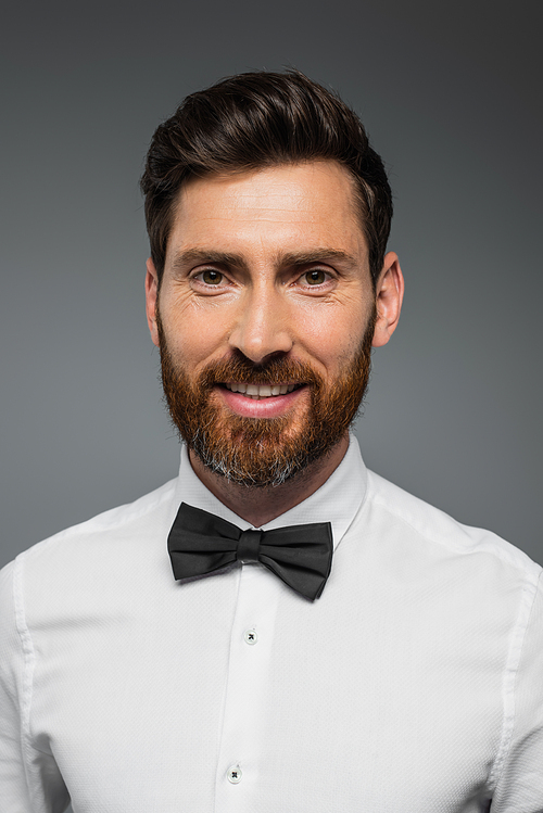 portrait of bearded man in white shirt with bow tie smiling isolated on grey