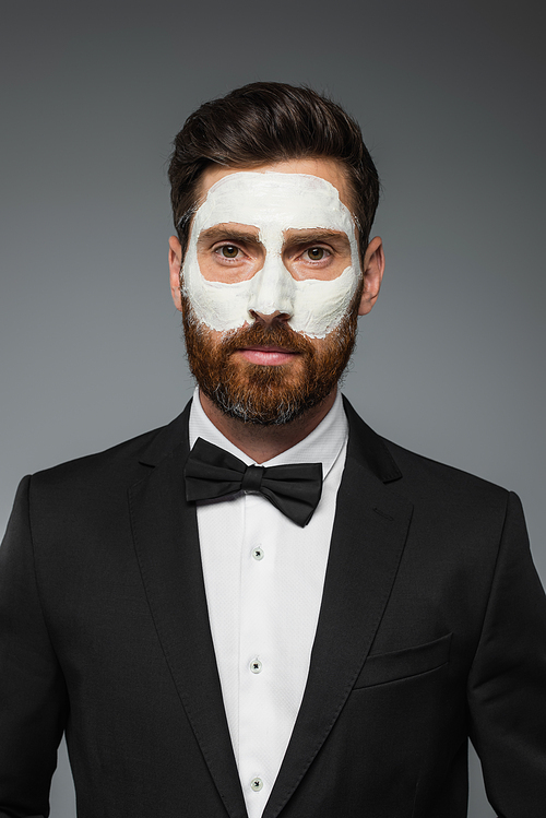 portrait of bearded man in tuxedo with clay mask on face isolated on grey