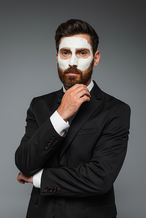 portrait of bearded man in suit with clay mask on face isolated on grey