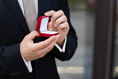 Cropped view of man in suit holding box with engagement ring outdoors