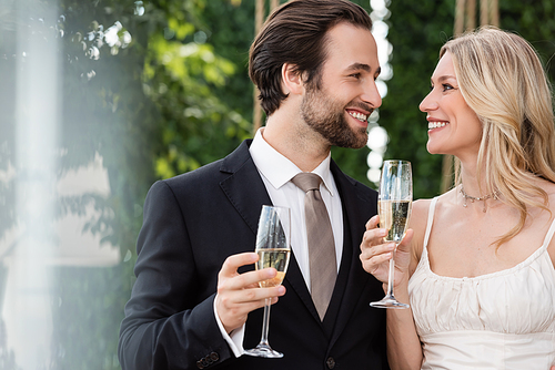 Cheerful newlyweds holding glasses of champagne outdoors