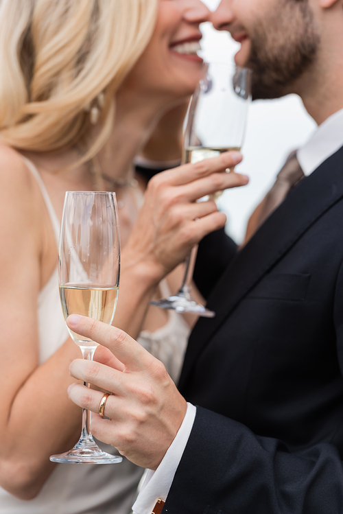 Cropped view of champagne in hand of groom kissing bride outdoors