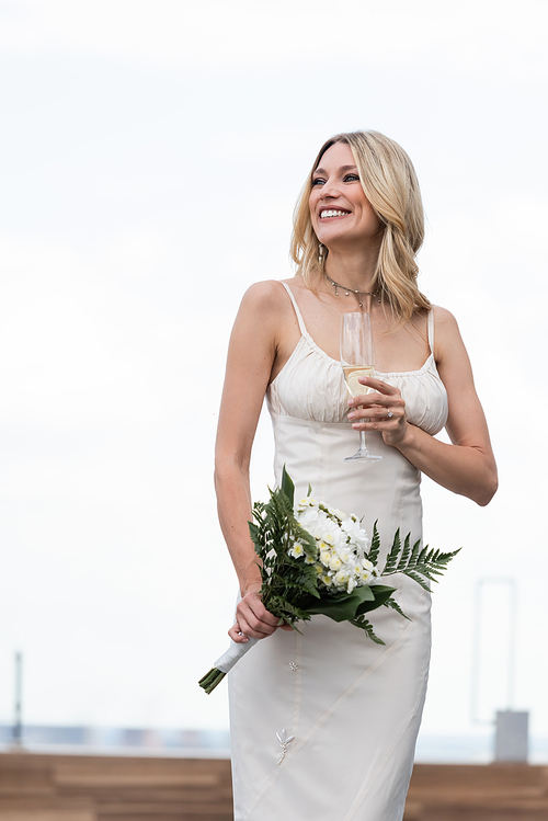 Blonde bride in wedding dress holding flowers and champagne outdoors