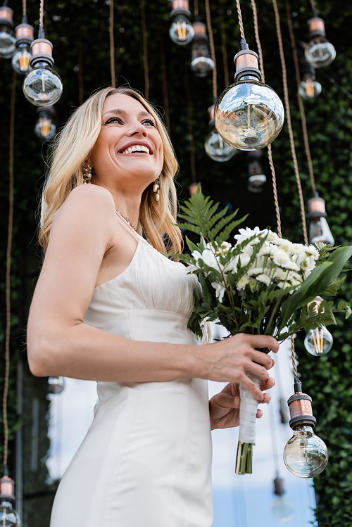 Low angle view of happy bride holding bouquet near light bulb on terrace