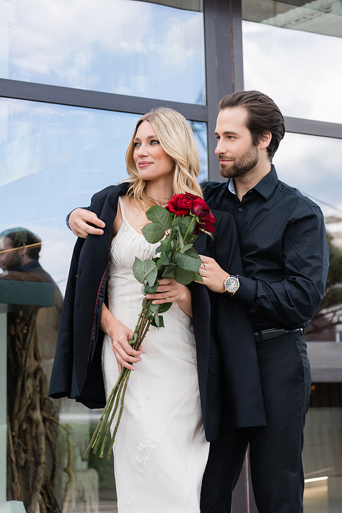 Elegant man wearing jacket on girlfriend with roses outdoors