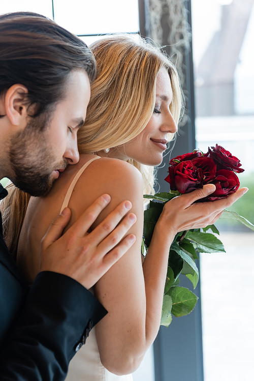 Side view of brunette man kissing smiling girlfriend with roses in restaurant