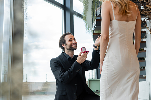 Smiling man holding box with engagement ring near girlfriend in dress in restaurant