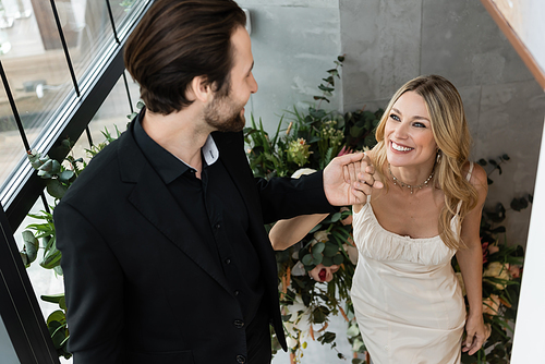 Young man in suit holding hand of happy girlfriend in dress smiling in restaurant