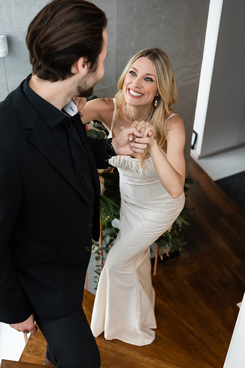 Smiling woman in elegant dress holding hand of boyfriend on stairs in restaurant