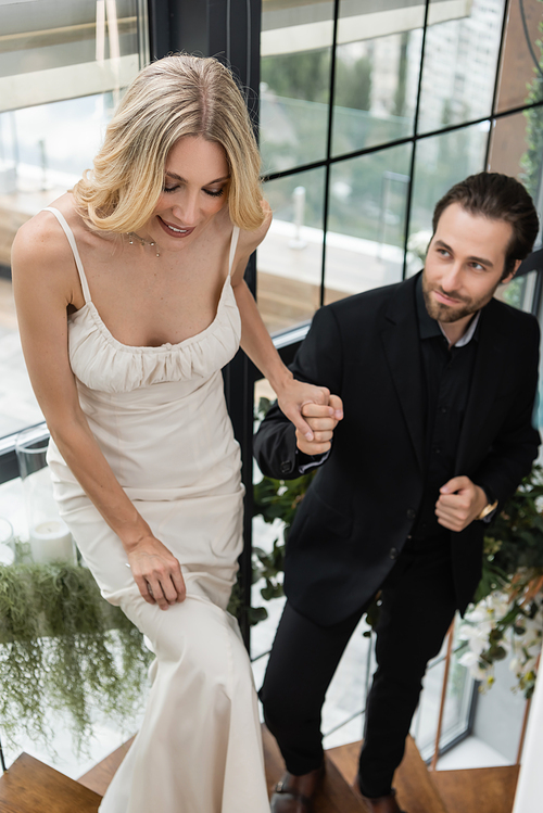 Smiling woman in dress holding hand of blurred boyfriend on stairs in restaurant