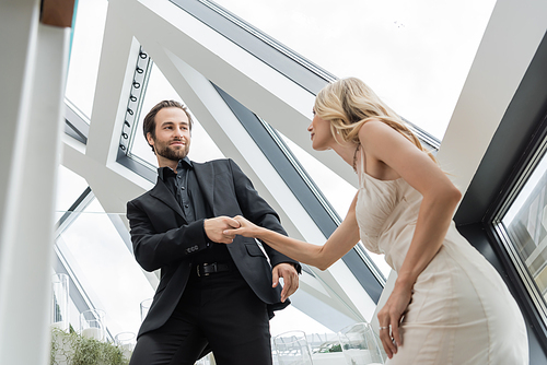 Low angle view of young man in suit holding hand of blonde girlfriend in restaurant