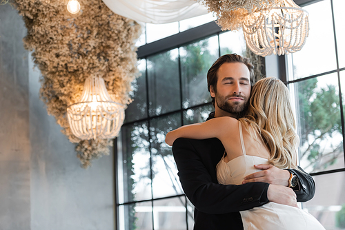 Bearded man in suit hugging blonde girlfriend in restaurant
