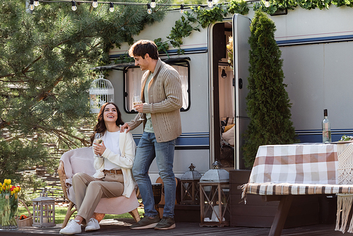 Smiling man in cardigan standing near girlfriend with wine and camper van