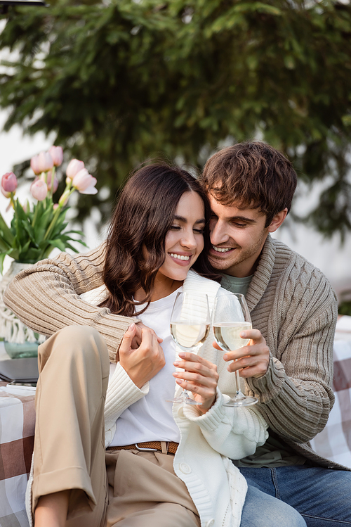 Positive man holding wine near brunette girlfriend in cardigan outdoors