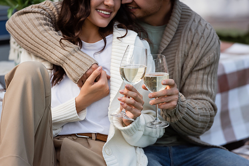 Cropped view of smiling couple in cardigans holding hands and glasses of wine outdoors