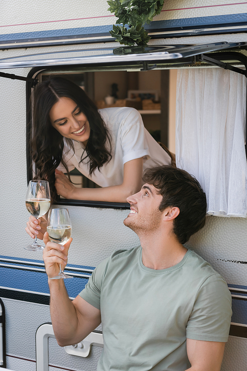 Smiling man holding glass of wine near girlfriend in camper van