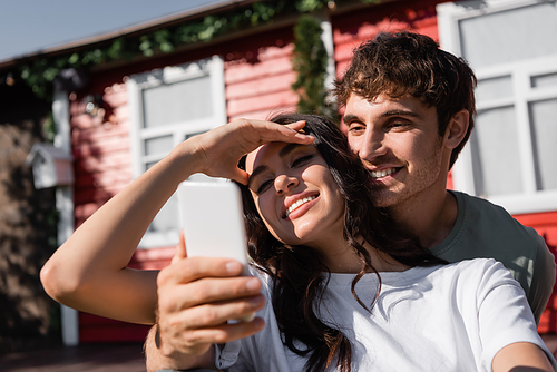 Smiling couple using smartphone near blurred house outdoors