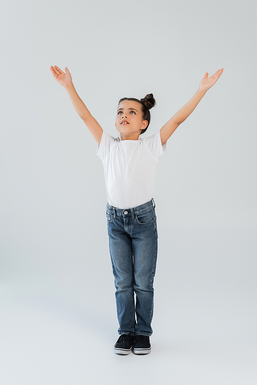 full length of adorable girl with sparkling glitter stars on cheeks standing with outstretched hands on grey