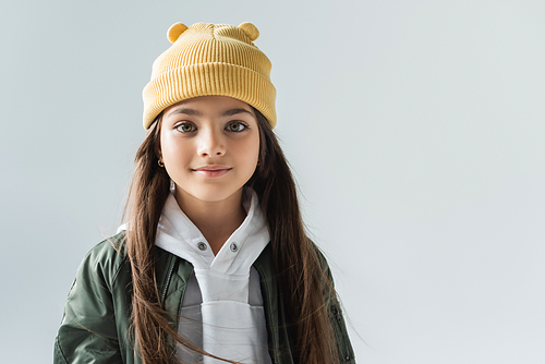 portrait of cheerful kid in yellow beanie hat and bomber jacket looking at camera isolated on grey