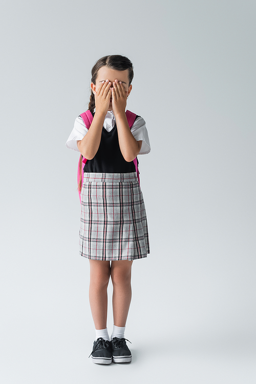 full length of girl in school uniform covering face while standing on grey