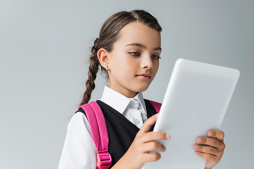 cute girl in school uniform with backpack using digital tablet isolated on grey