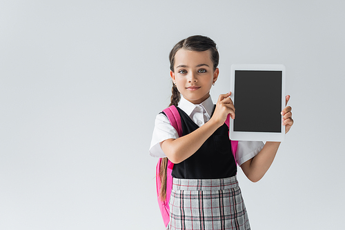 cute schoolgirl in uniform holding digital tablet with blank screen and smiling isolated on grey