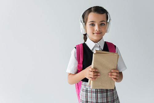 girl in school uniform and wireless headphones holding books isolated on grey