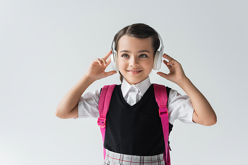 cheerful schoolgirl in wireless headphones listening music isolated on grey