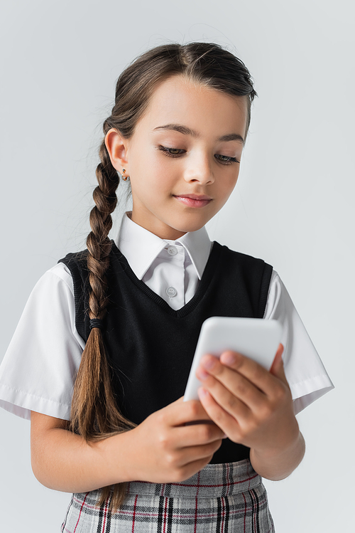 cute girl in school uniform using smartphone isolated on grey