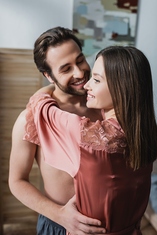 happy young woman in pink silk robe hugging cheerful man
