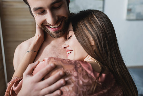 bearded and happy man hugging tattooed girlfriend in pink silk robe
