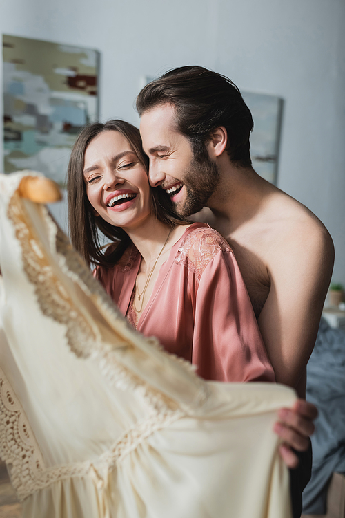 bearded and happy man laughing with girlfriend holding blouse