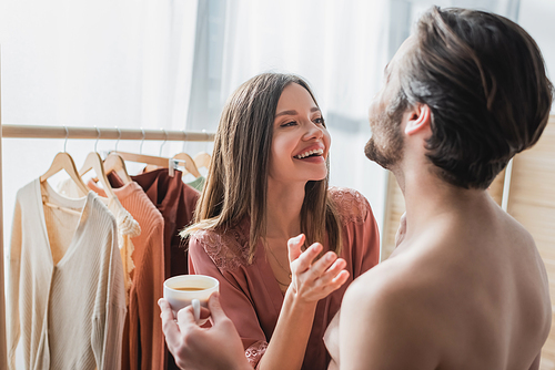 happy man holding cup of coffee near cheerful woman laughing at home