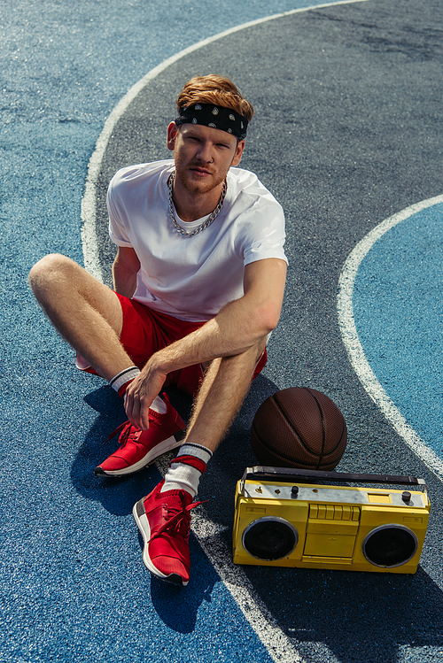 high angle view of young basketball player sitting on court near ball and tape recorder