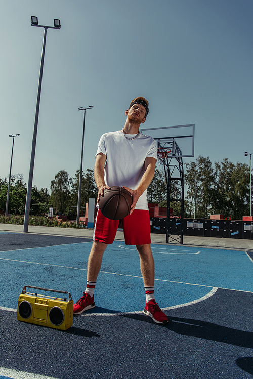 full length of basketball player standing near boombox with ball