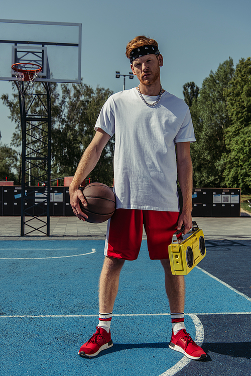 young basketball player with ball and boombox looking at camera on court