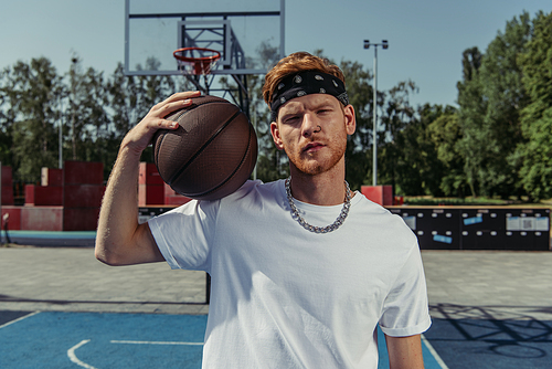 basketball player in bandana and necklace holding ball and looking at camera