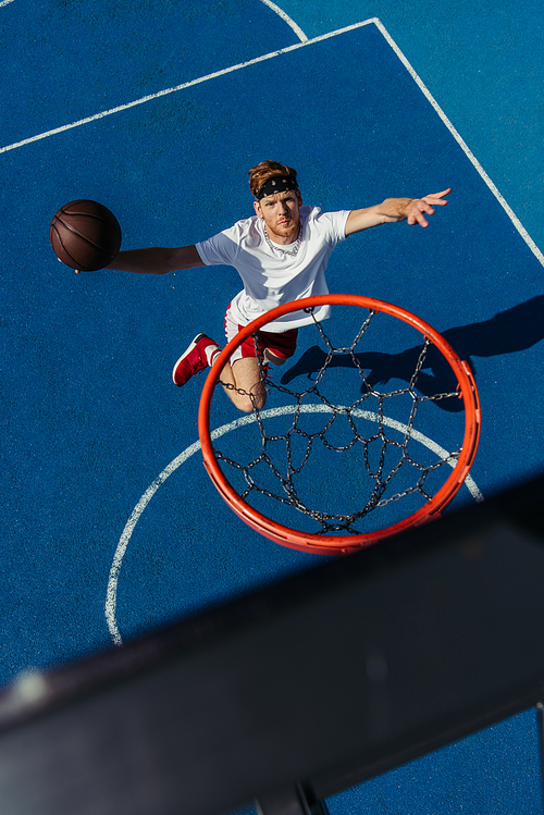 top view of young sportsman jumping with ball under basketball ring