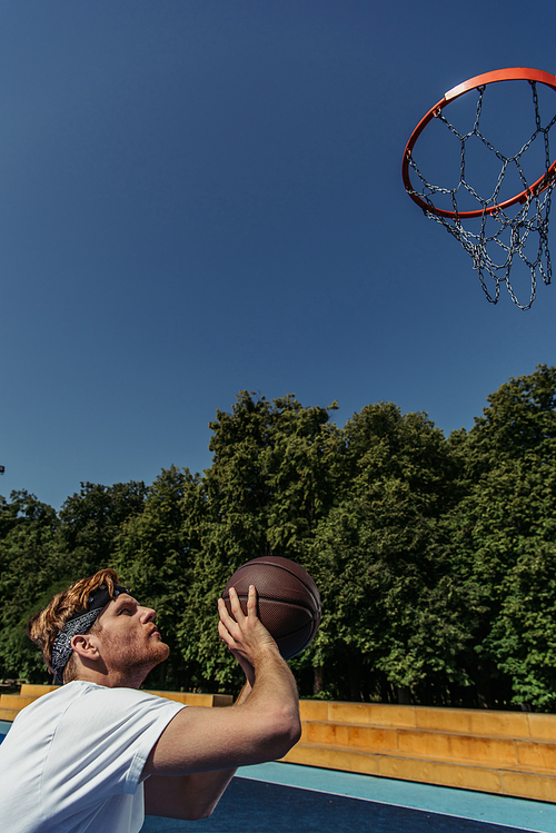 side view of redhead man in bandana playing basketball outdoors