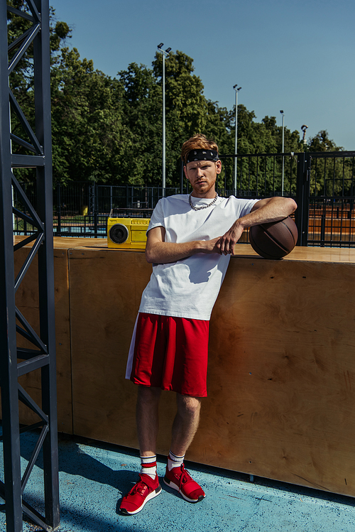 full length of basketball player in red shorts standing near boombox and looking at camera