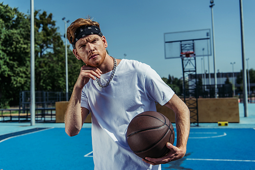 sportive man in necklace and bandana holding ball and looking at camera