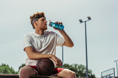 young basketball player drinking water from sports bottle while sitting outdoors