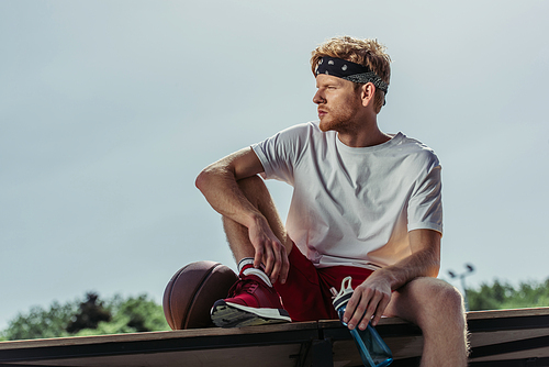 basketball player with sports bottle and ball looking away outdoors