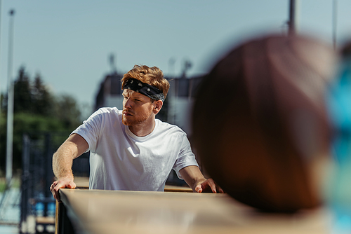 redhead sportsman in bandana looking away near blurred ball